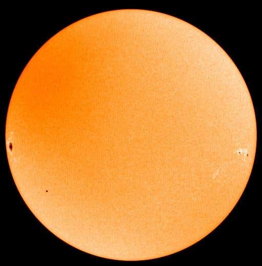 Mercury appears as a miniscule black spot at lower left, dwarfed by a large sunspot at mid left in this visible light SOHO image. Two more sunspots appear at mid right