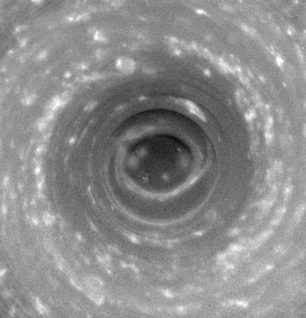 A hurricane-like vortex swirls on Saturn's south pole, where towering clouds cast shadows around them 