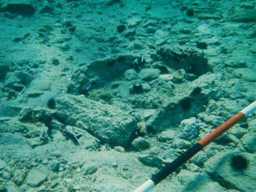 Rectangular cist grave made by four stones standing on edge. The markings on the range pole are in 25-centimetre bands