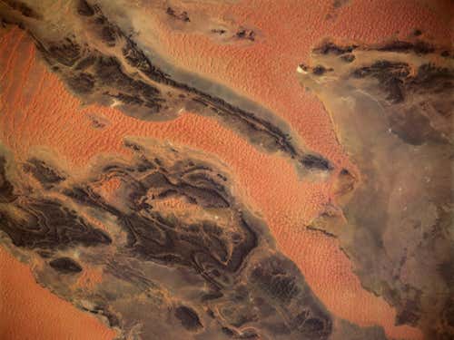 A view from space: regions of sand dunes are broken up by large expanses of desert varnish in Kahal Tabelbala, Algeria