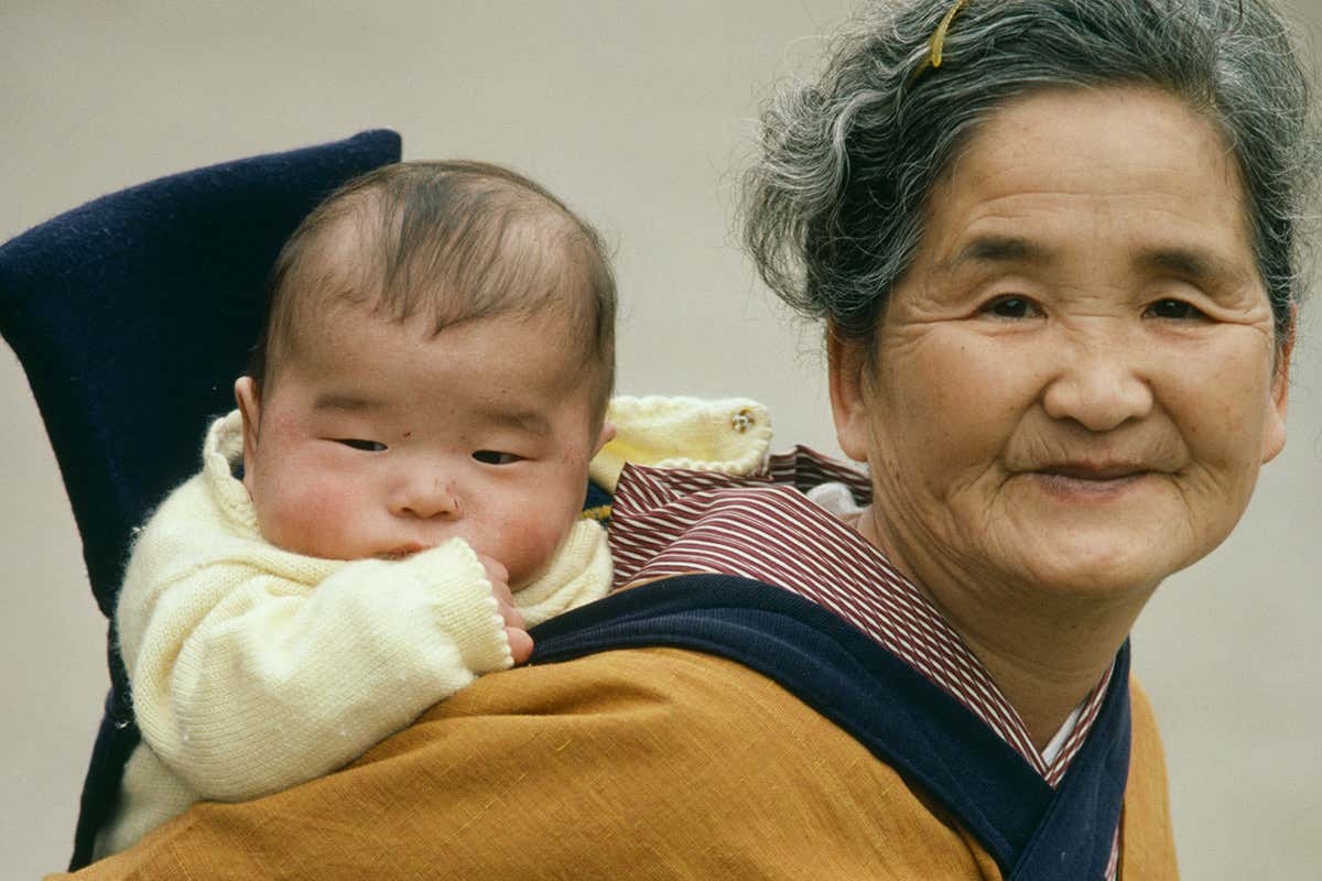 An older Japanese woman carrying a baby on her back
