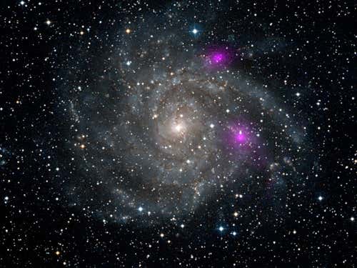 Two black holes, coloured magenta, spewing out X-rays in the outskirts of spiral galaxy IC 342