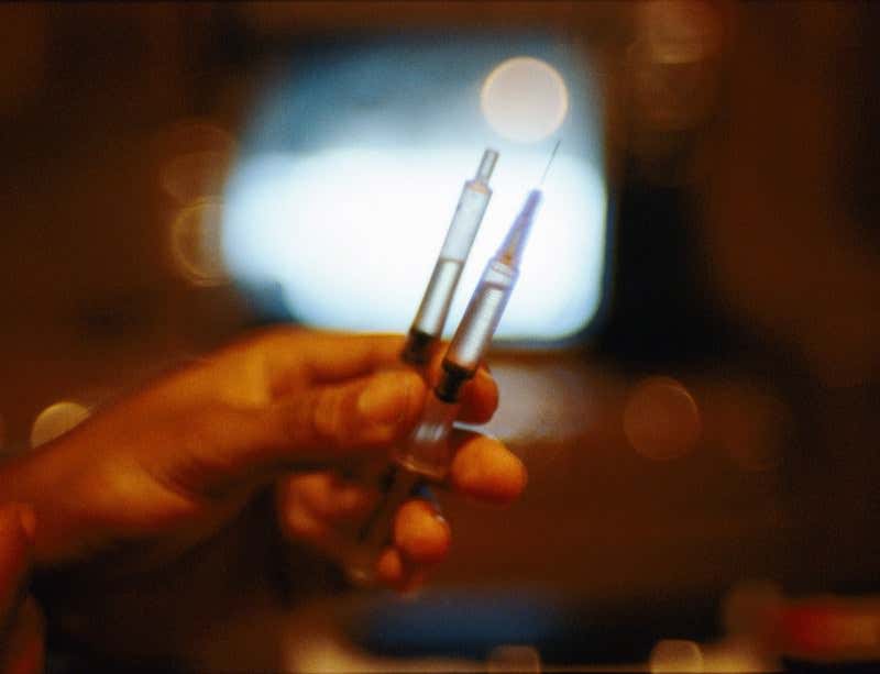 A hand holding two hypodermic syringes