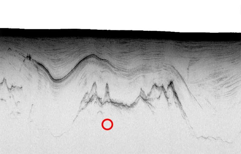 Radio waves reflected from the features beneath the ice show an undulating layer of ash (middle black line) above the craggy bedrock (bottom black line). The tremors occurred much deeper but the red circle shows their horizontal position. The black line at the top is the surface of the ice 