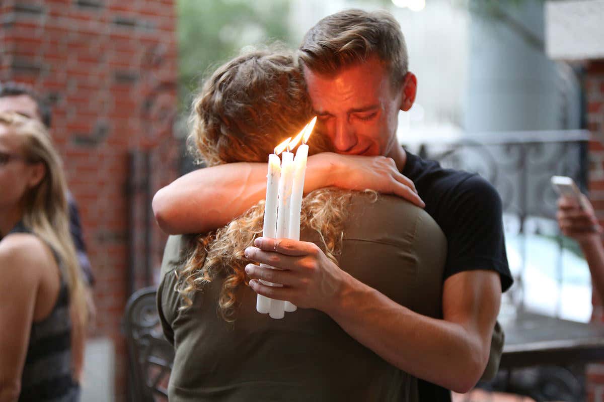 A person holding three lit candles cries while being embraced at a gathering to remember victims of an attack on the Pulse nightclub in Orlando, Florida