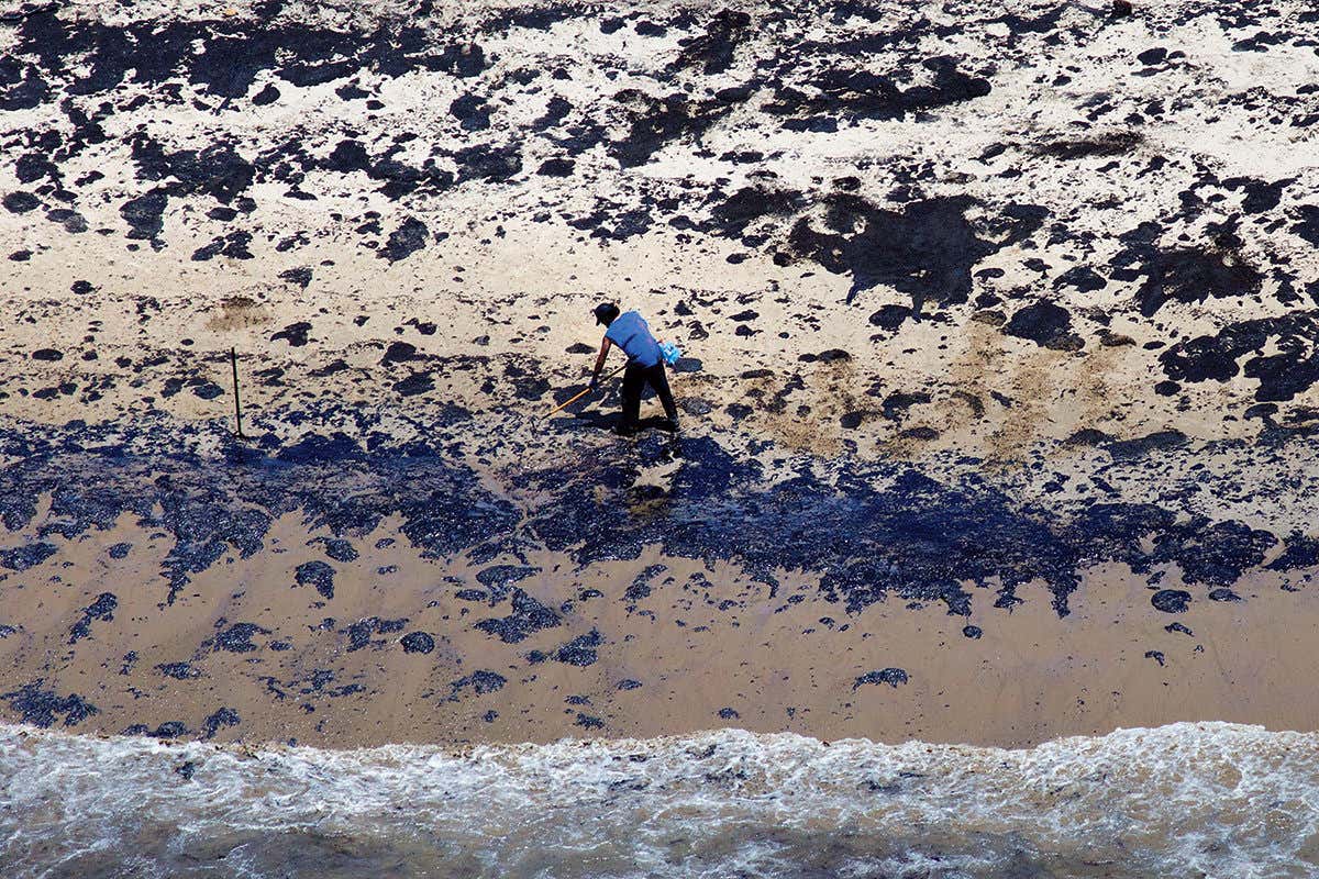 Overhead view of the oily surface of a beach, with a person clearing up