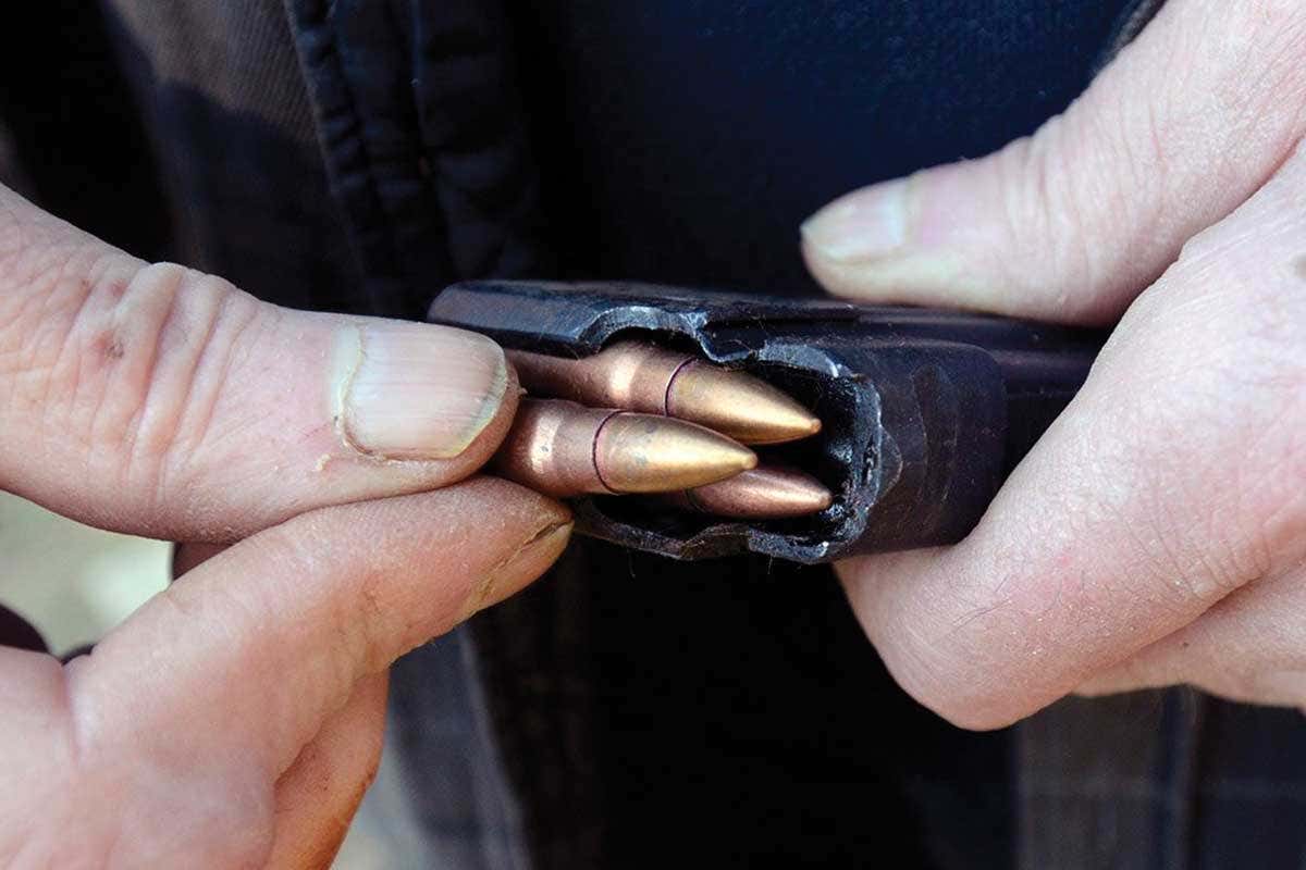 Close-up of someone's hand taking out some copper-coloured, mean-looking pointy bullets from a case