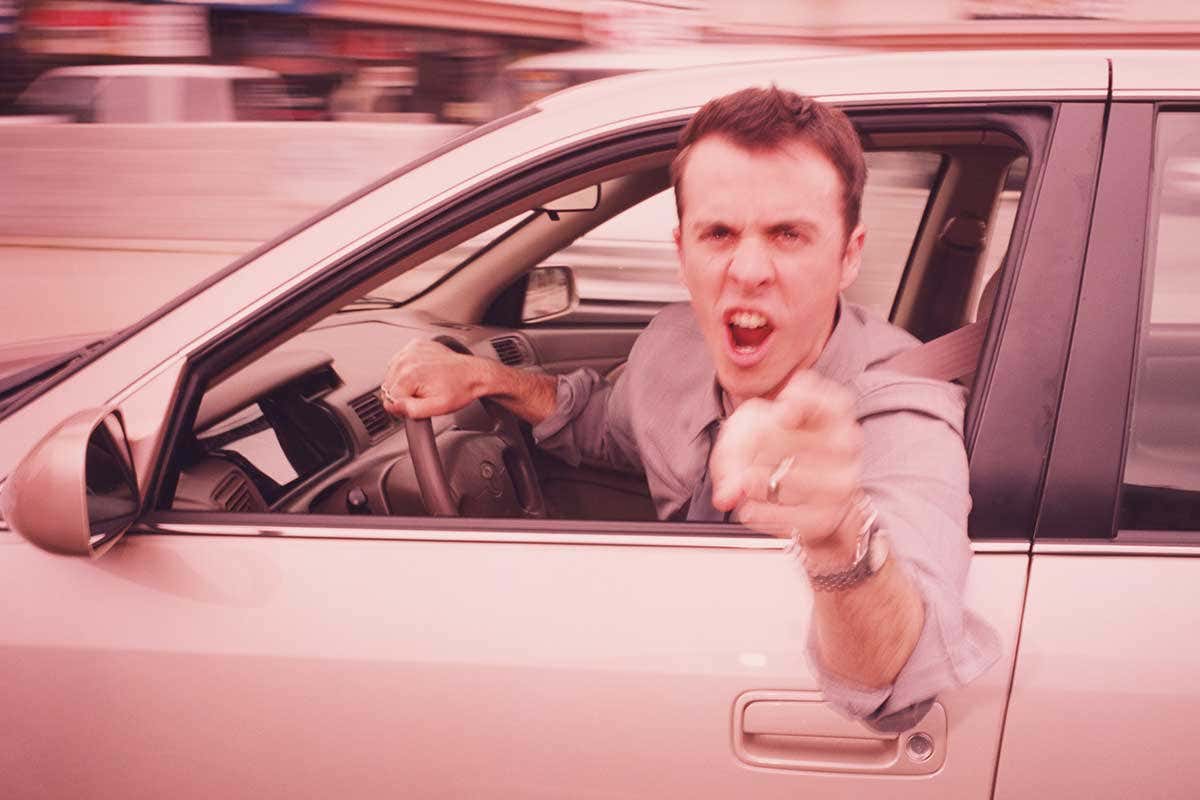 An angry man leaning out of a car and gesticulating at the camera
