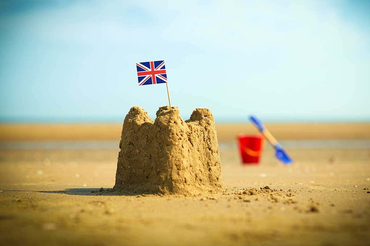 A sandcastle with Union Jack in it and a bucket and spade near by on the beach
