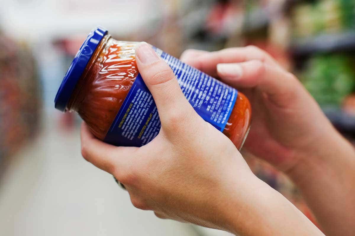 Someone is inspecting the label on a jar of processed sauce