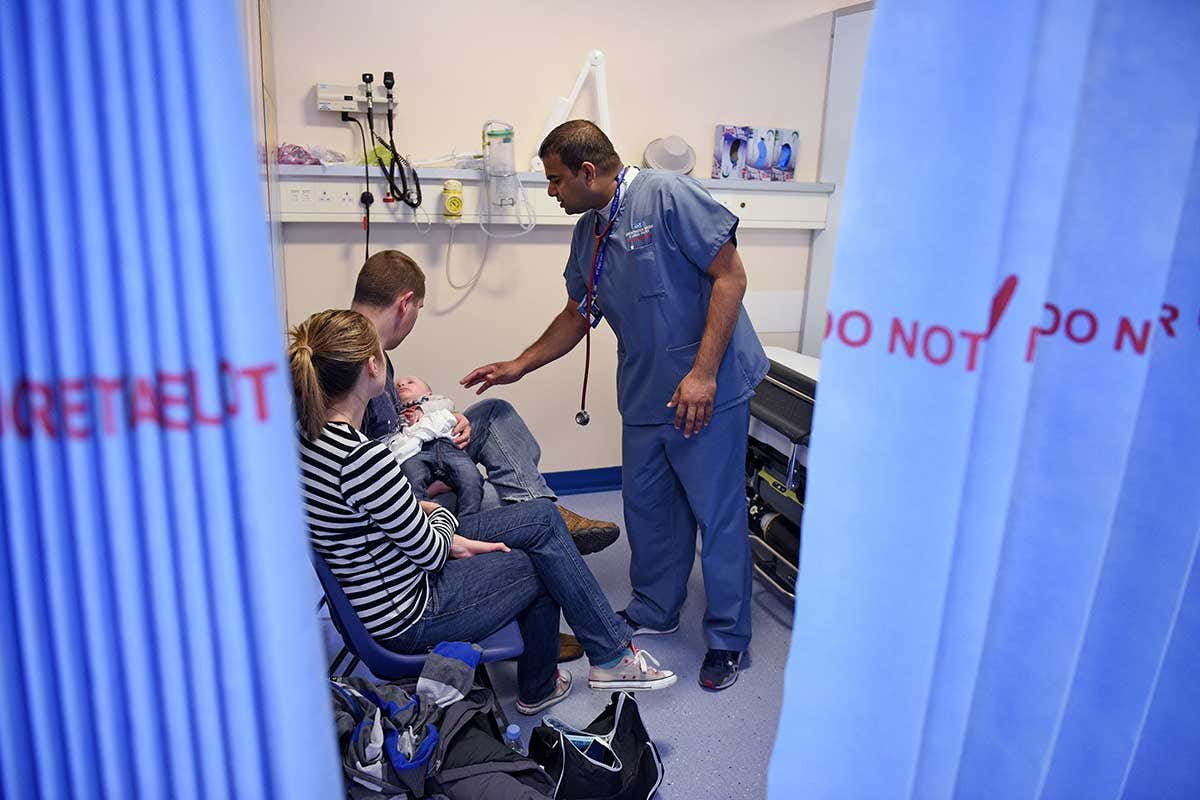 Some parents and a baby being looked at in an A and E cubicle by a doctor in scrubs