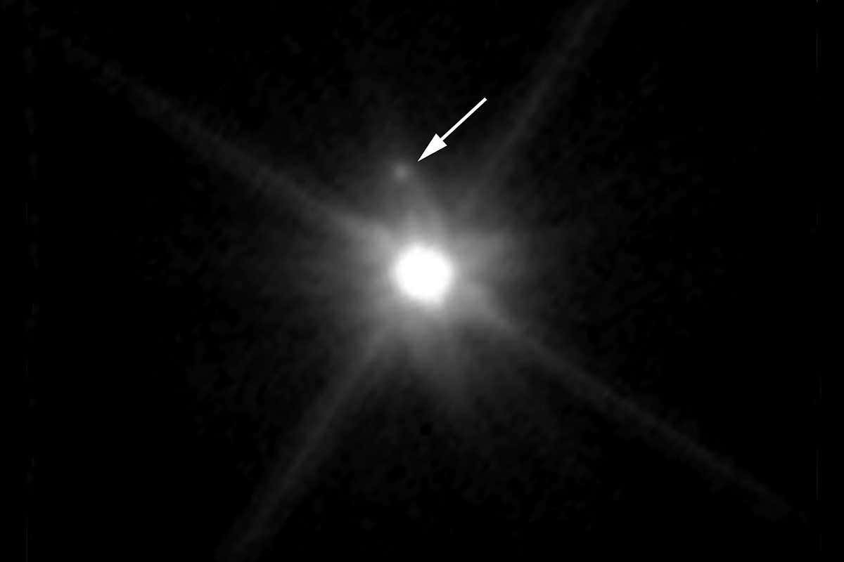 Makemake shining brightly, with a small, faint blob just above it and a big arrow pointing to it