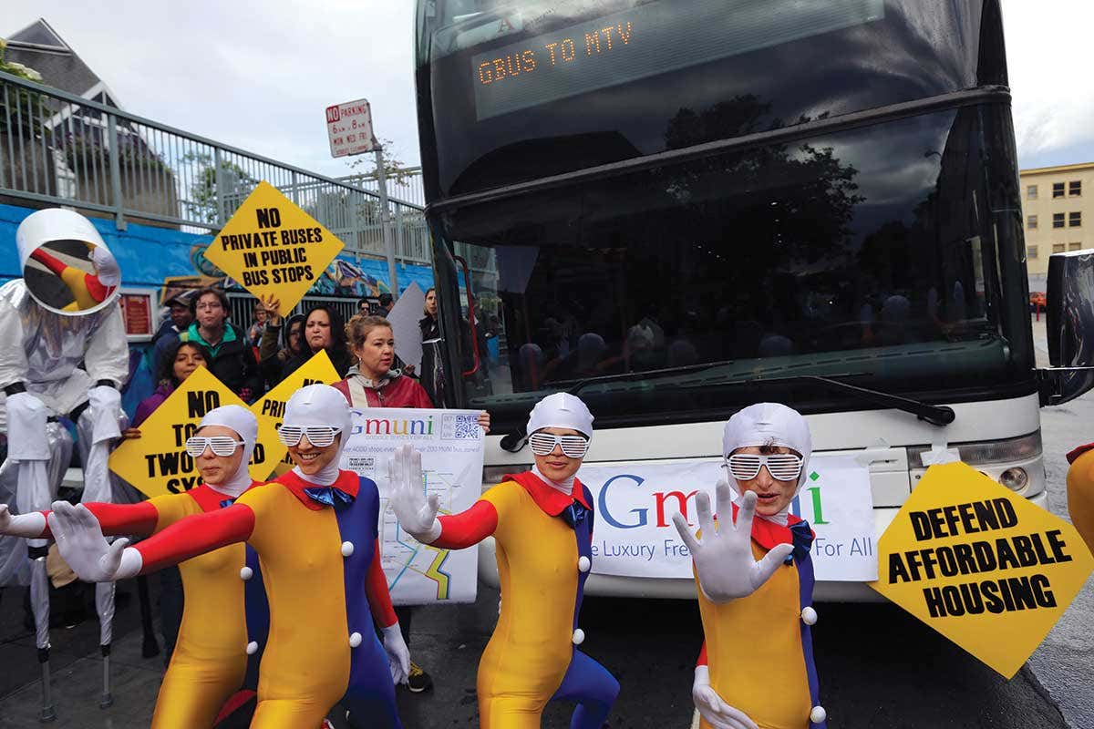 Protesters in colourful outfits stand in front of a bus that says Gbus to MTV on it