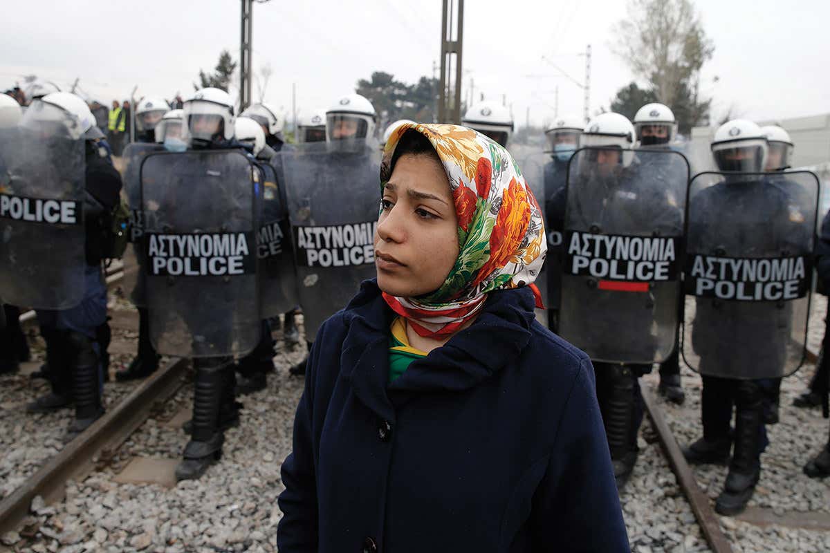 Woman in headscarf waits in front of police bearing riot shields