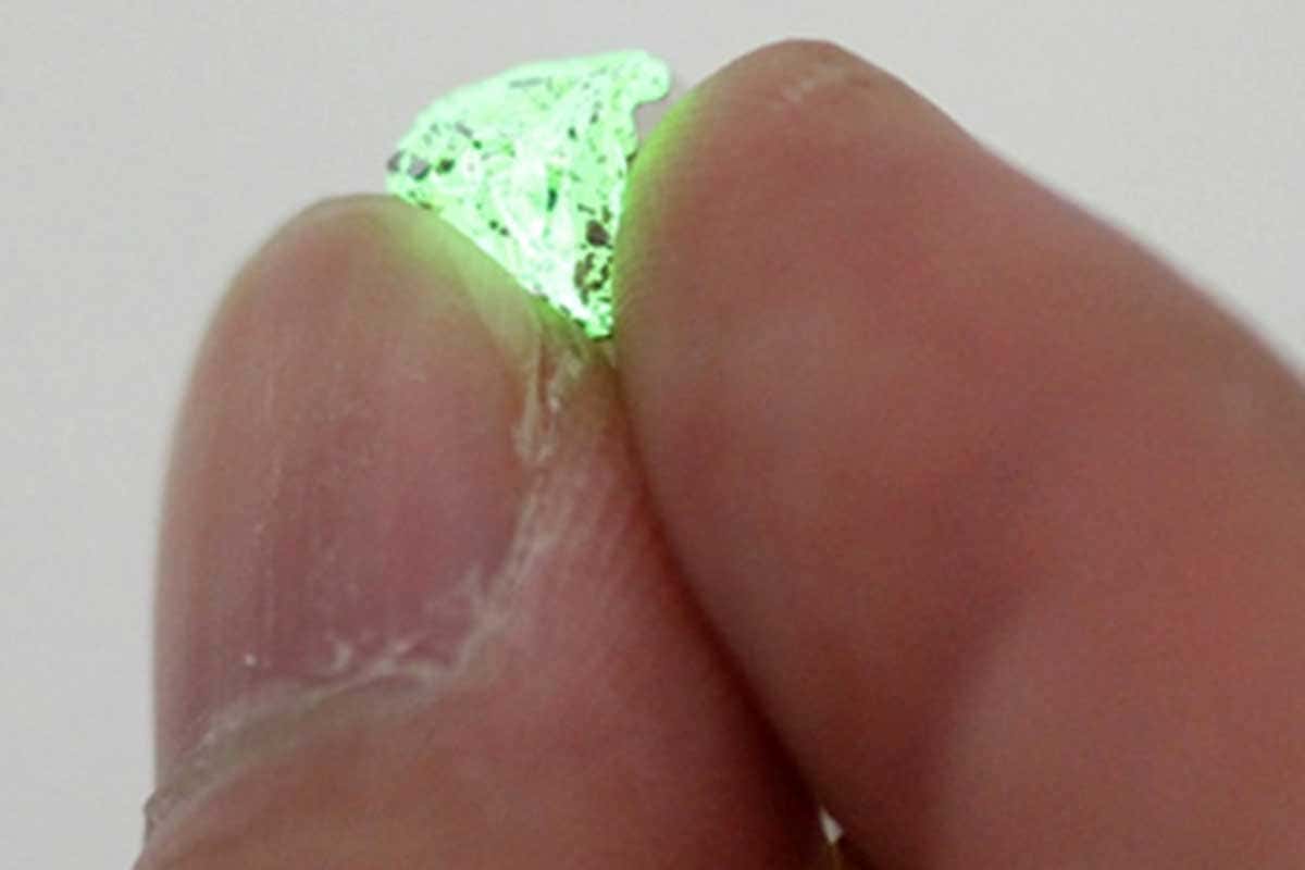 Fingertips holding glowing green crystal