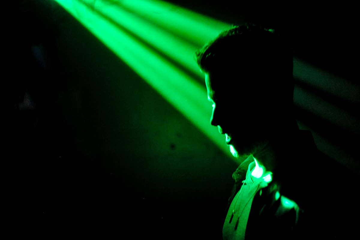 A ray of bright green light shining on a person in silhouette on a black background