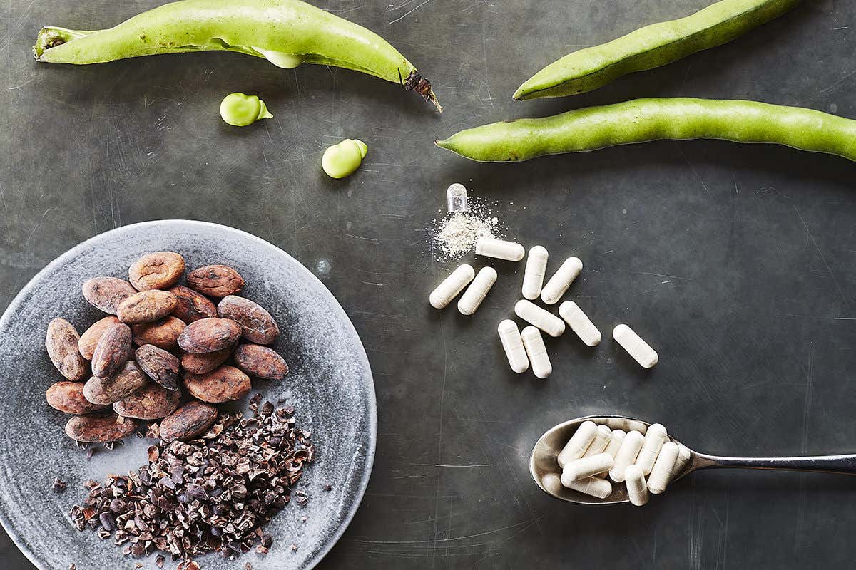 Some broad beans, nuts and seeds arranged on a table beside a handful of white capsules