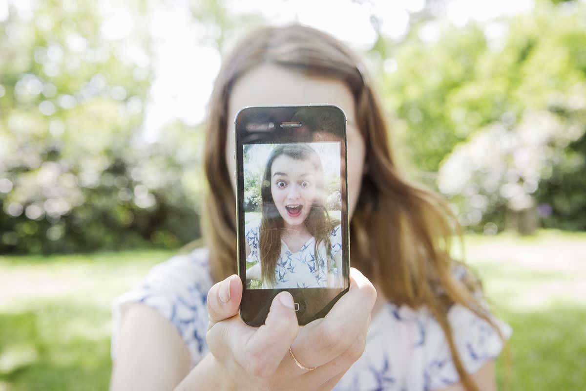 Woman holding smartphone in front of her face, with her face displayed on the phone