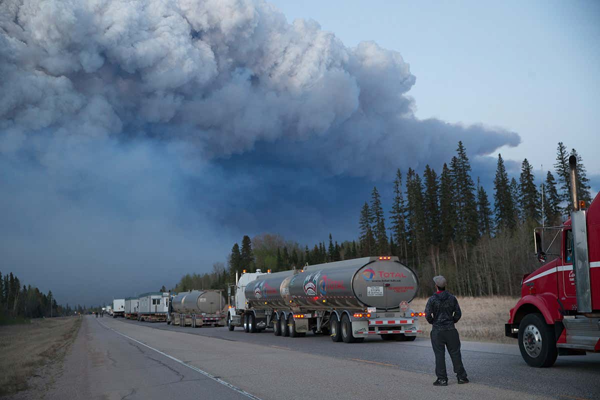Long line of traffic with massive smoke plume above forest