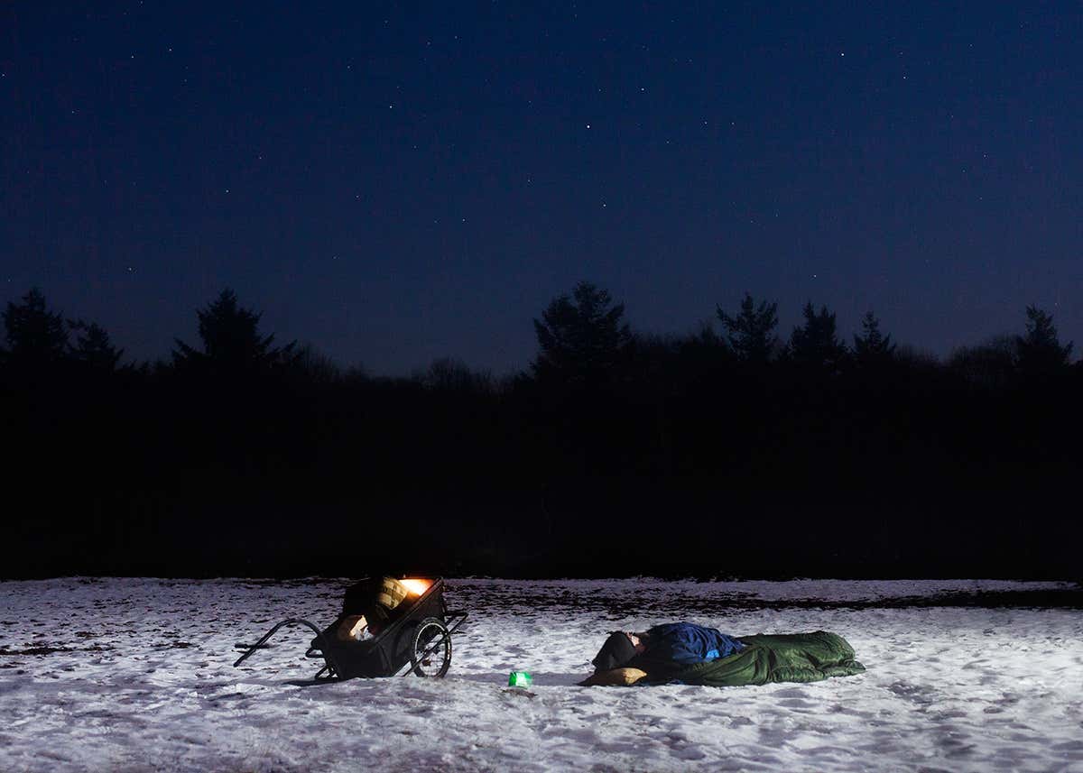 Man in sleeping bag lying on snow looking up at the night sky