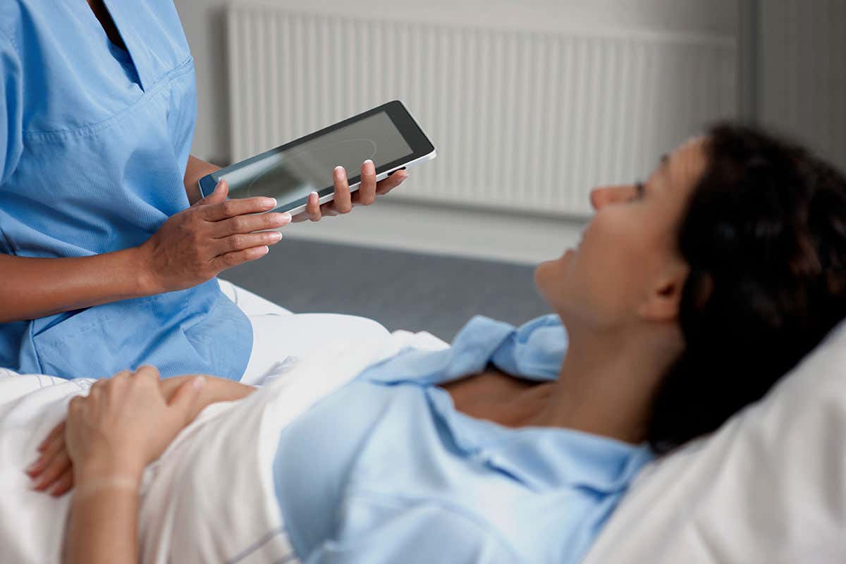 A woman in a hospital bed with clinician standing by
