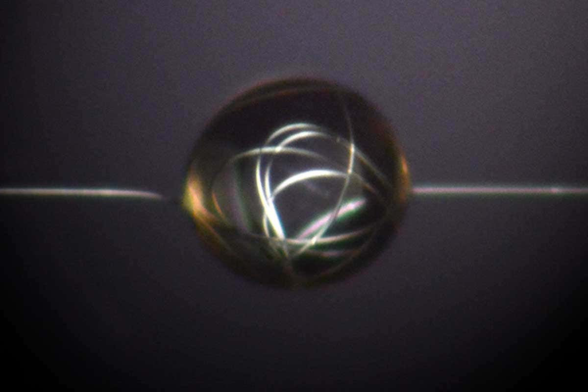 A transparent ball of glue, close up, with a white strand of spider silk going into it, twirling around and comnig out the other end. Looks cool and abstract