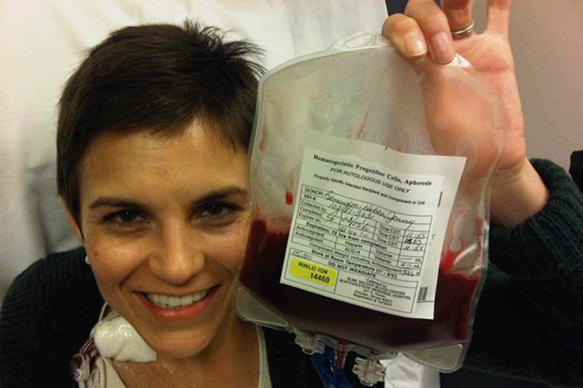 The person in question smiliing and holding up a blood bag