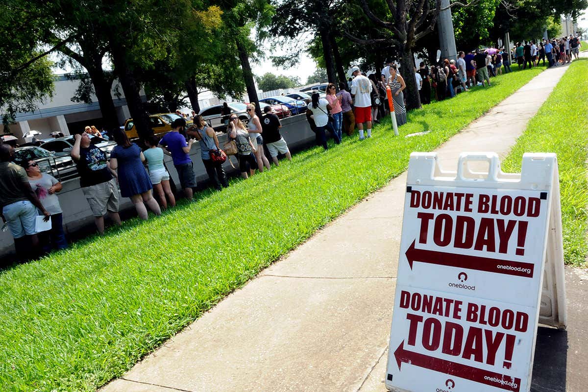 A queue of people waiting to give blood beside a sign saying
