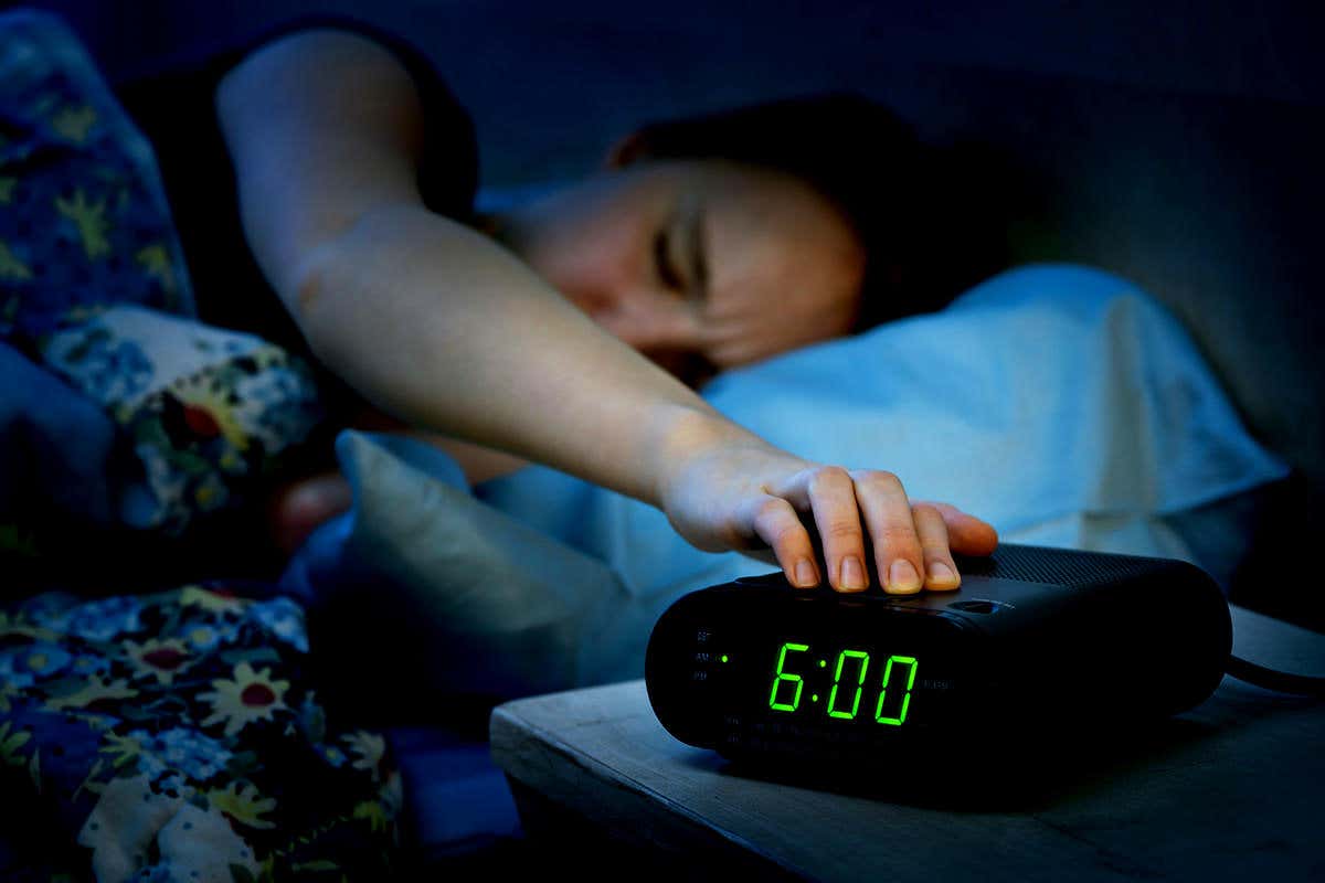 Young woman pressing snooze button on early morning digital alarm clock radio
