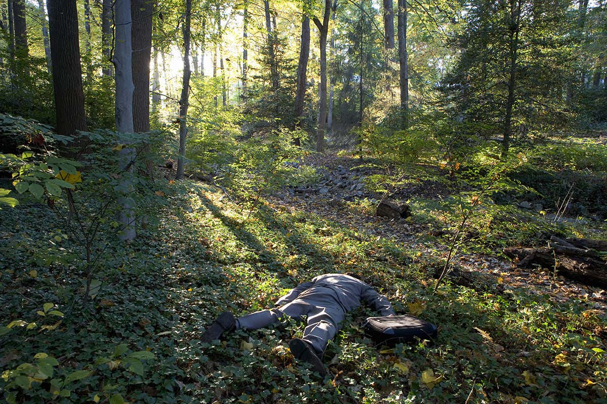 Man in suit lying face down in a forest