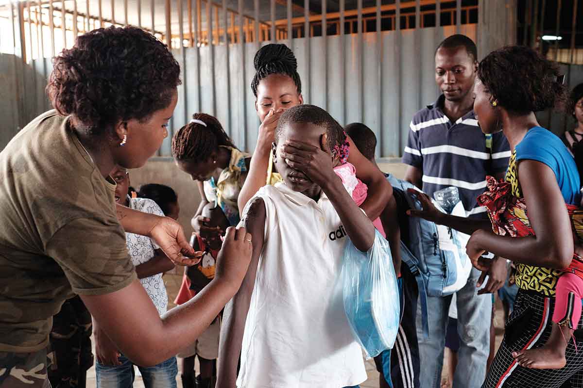 Angolan child covers eyes while being vaccinated
