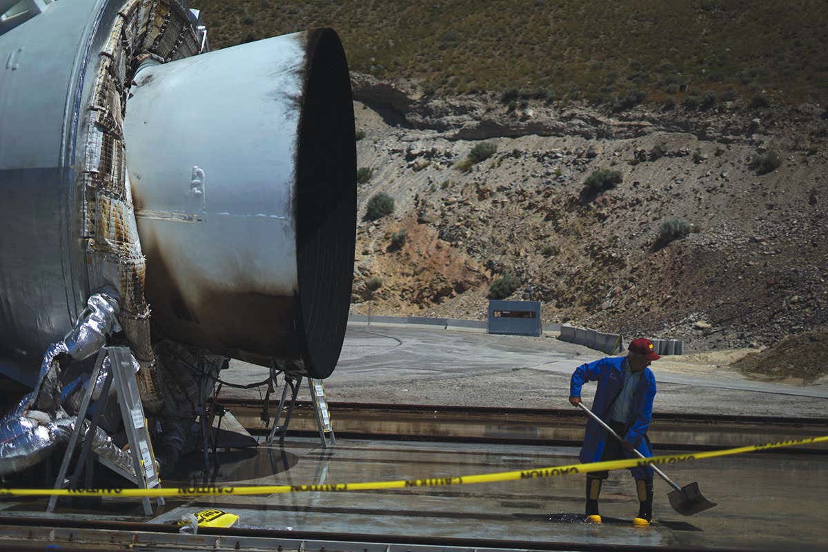 Man in blu coat appears to be tidying up behind the rocket exhaust