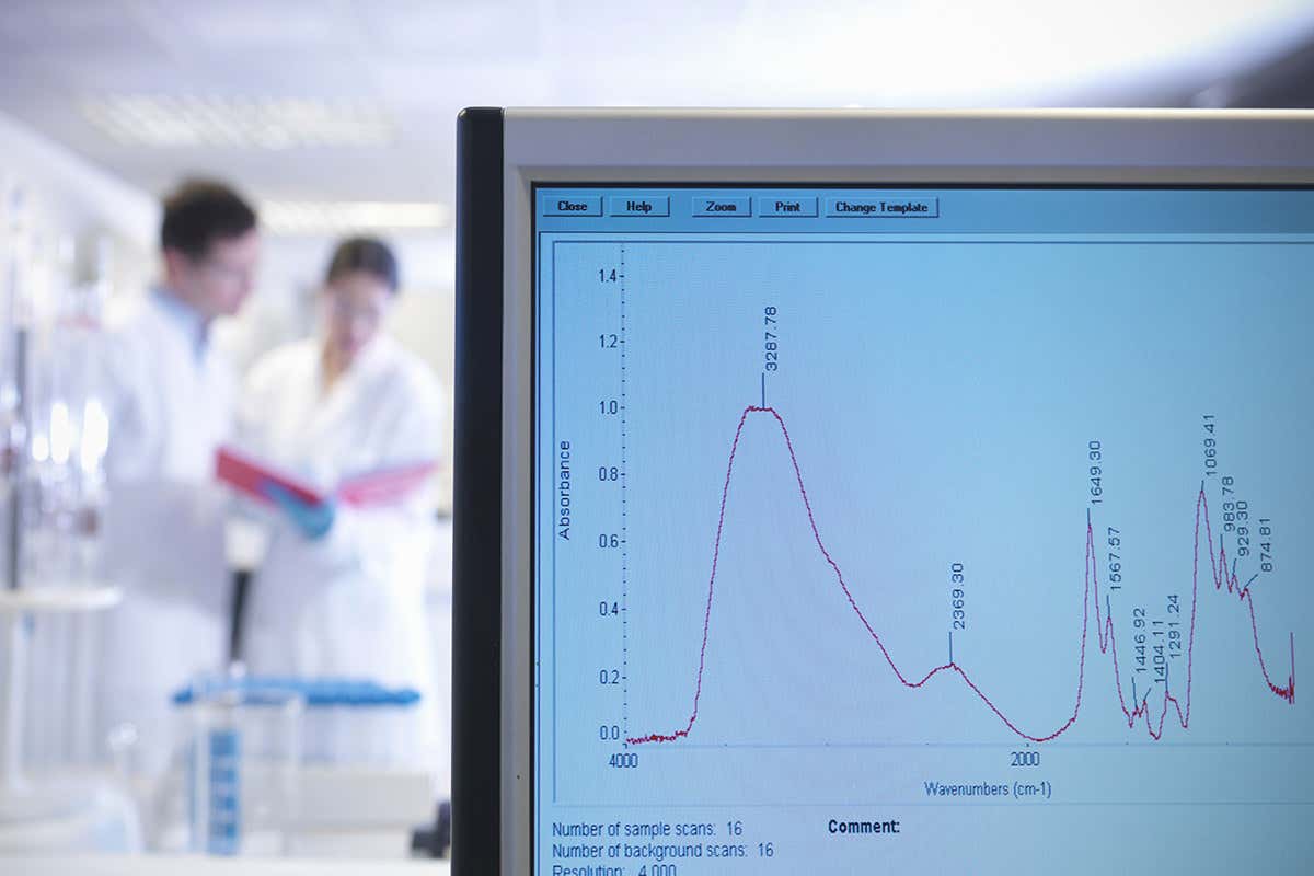 A graph of some results in the foreground with two scientist in lab coats inspecting data in the background