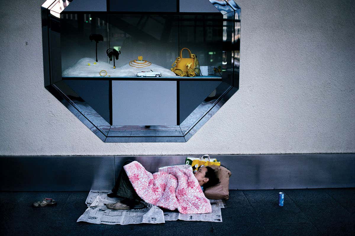 Person sleeping on pavement underneath luxury items window display