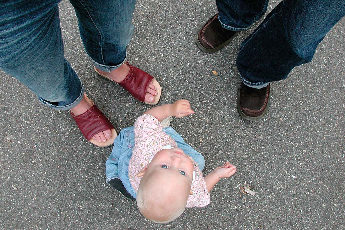 A toddler looking up with two adults' feet in the shot