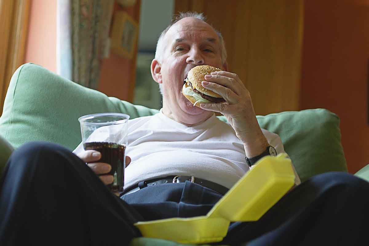 Old man eats burger on his sofa