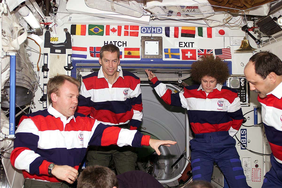 Astronauts on the International Space Station with many flags on panel behind them