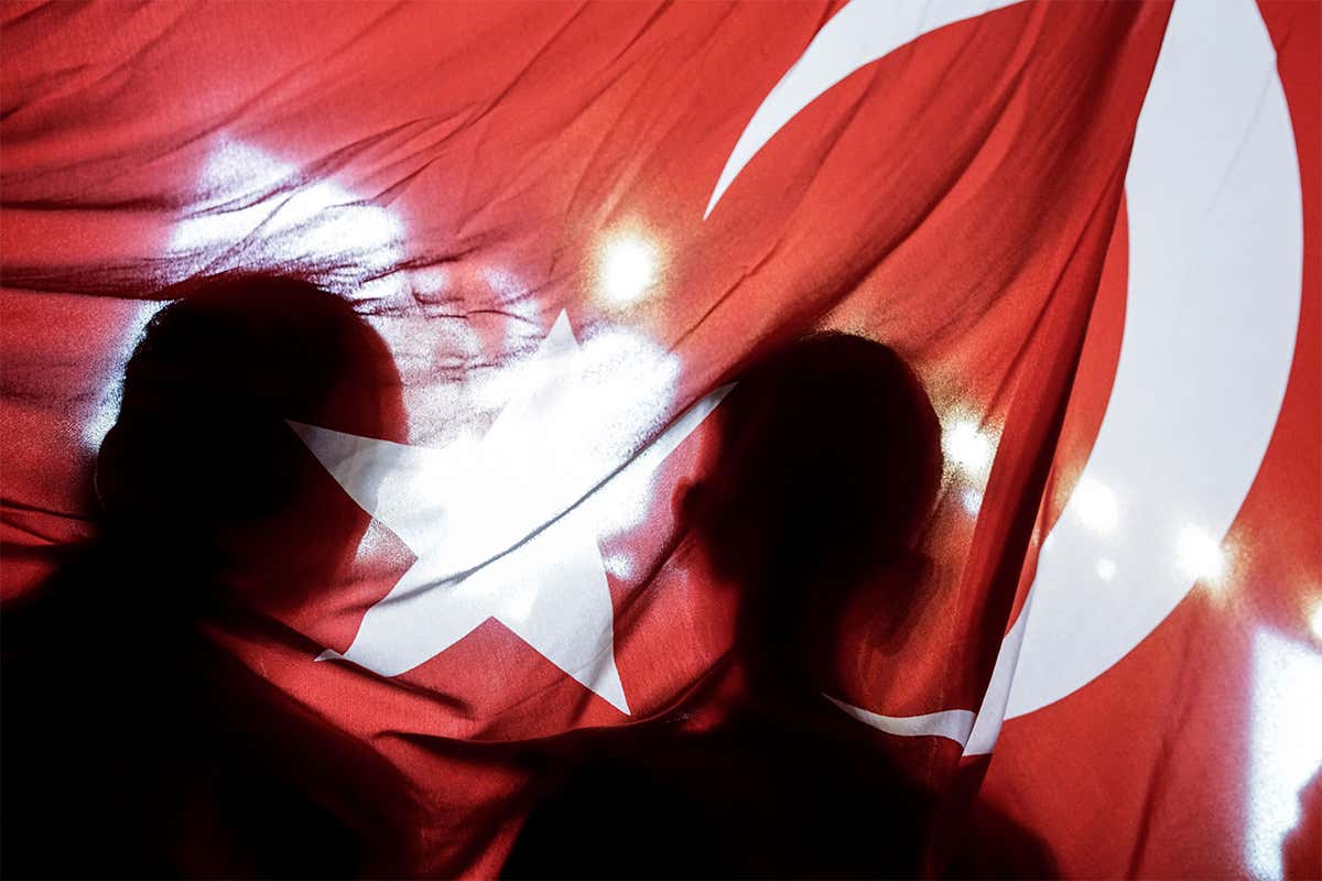 Two people silhouetted against the Turkish flag