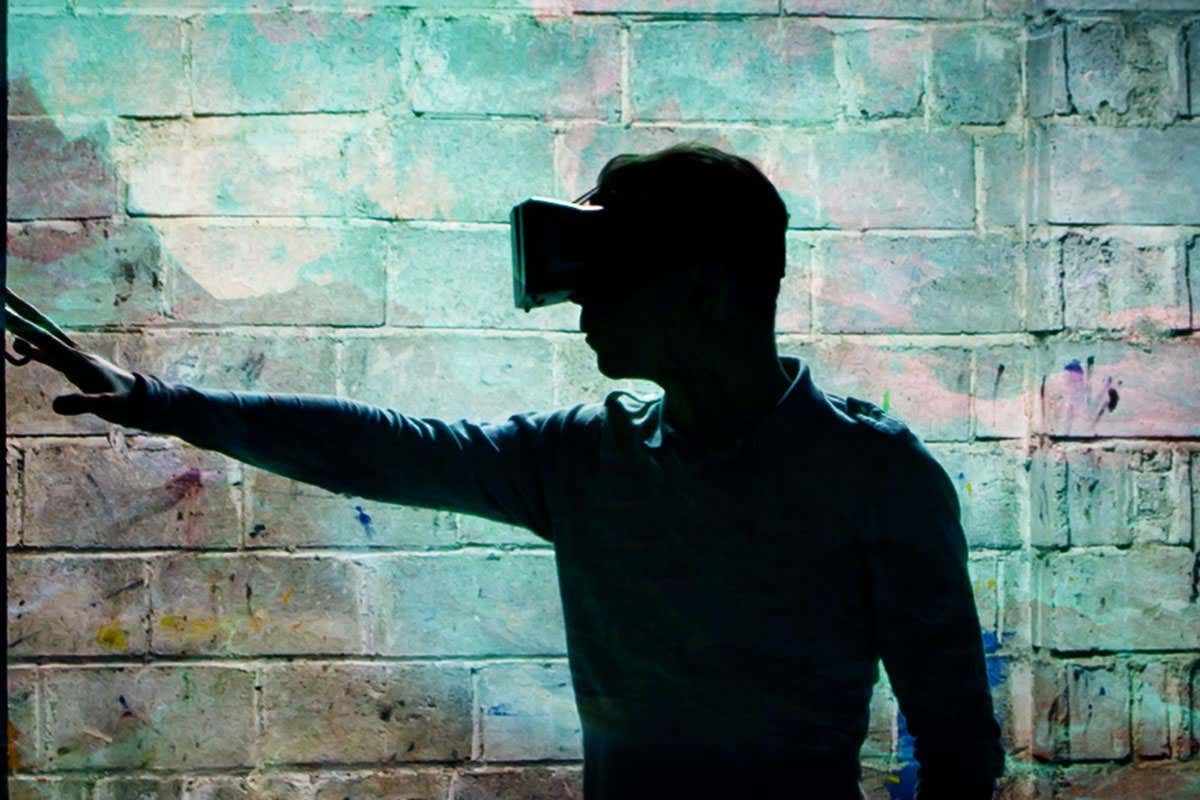 A person wearing a virtual reality headset stands in front of a brick wall with an arm outstretched