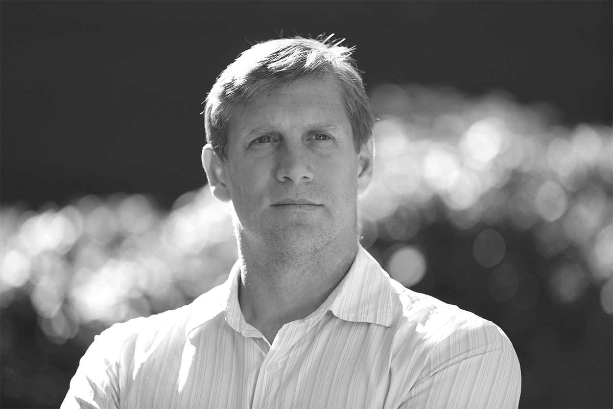 Zoltan Istvan, head and shoulders, pictured in black and white with clouds in the background. He's white, square-jawed and arrogant-looking