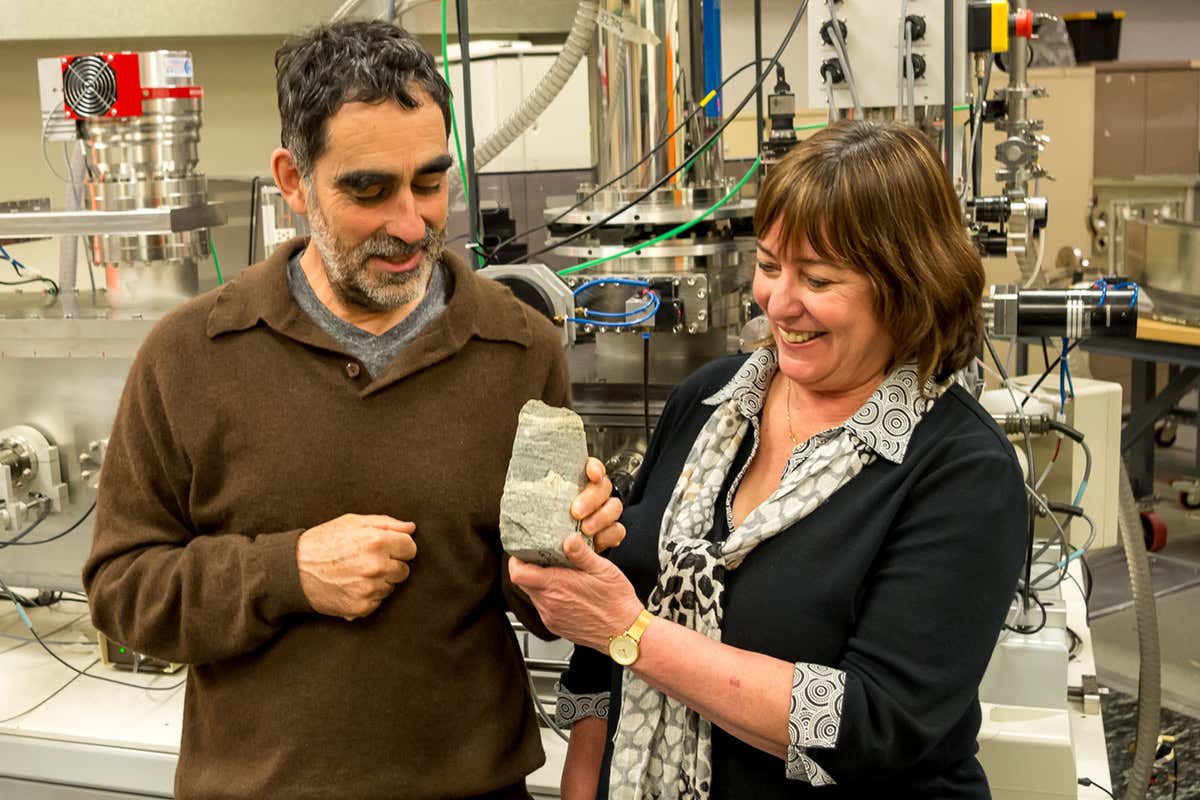 Two researchers holding up one of the pieces of rock in question. It has a wavy line on it that represents the putative fossil