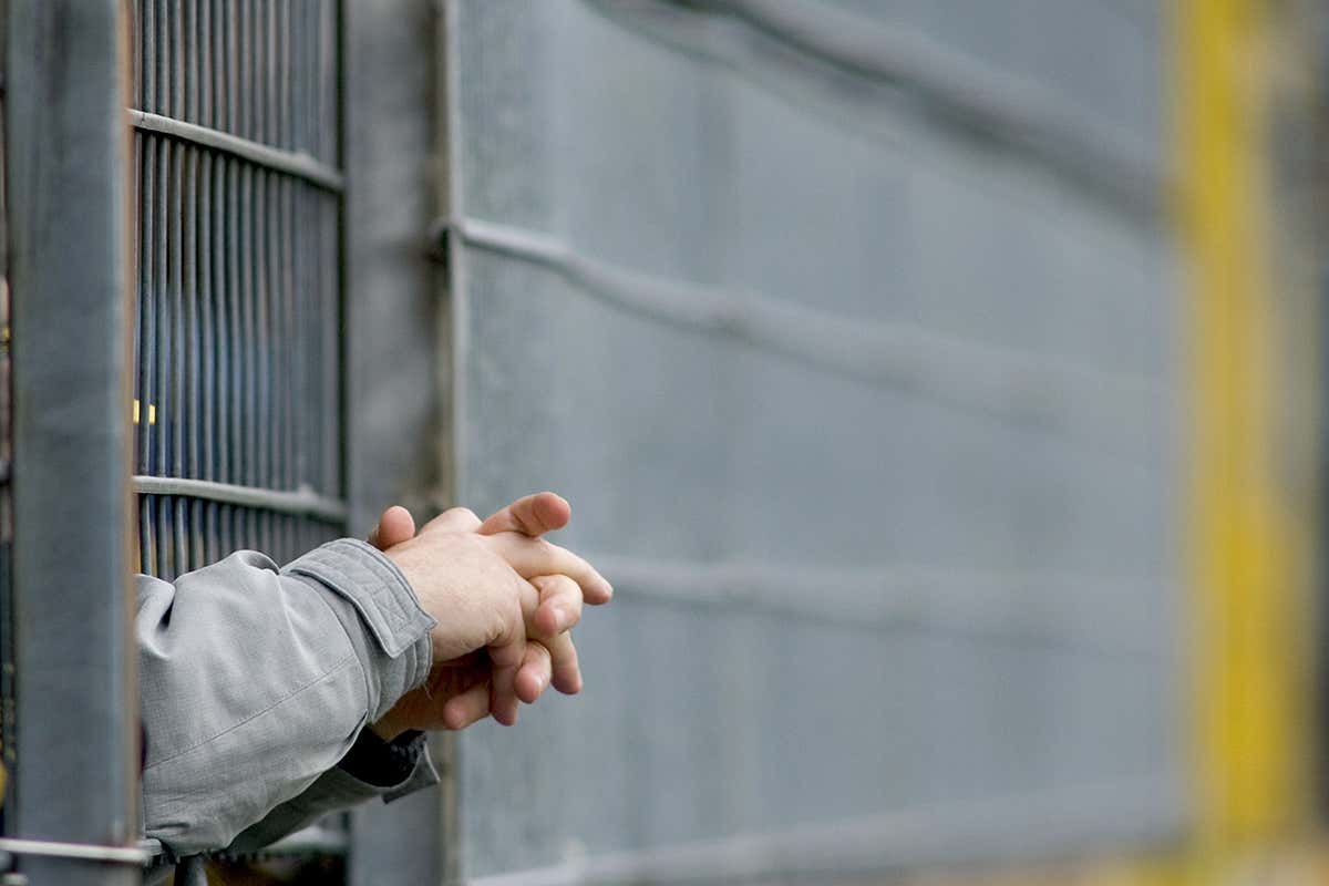 Hands extend through a barred door