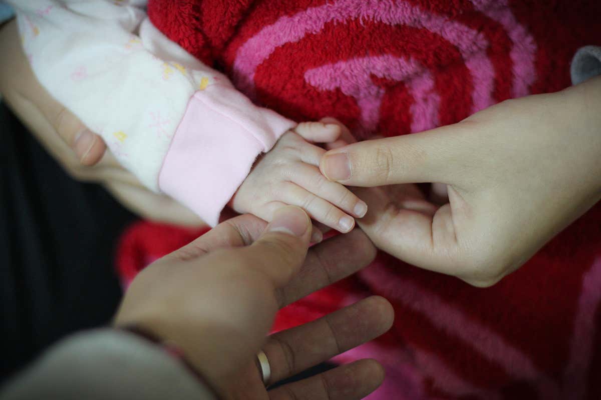 Three hands holding a baby's hand