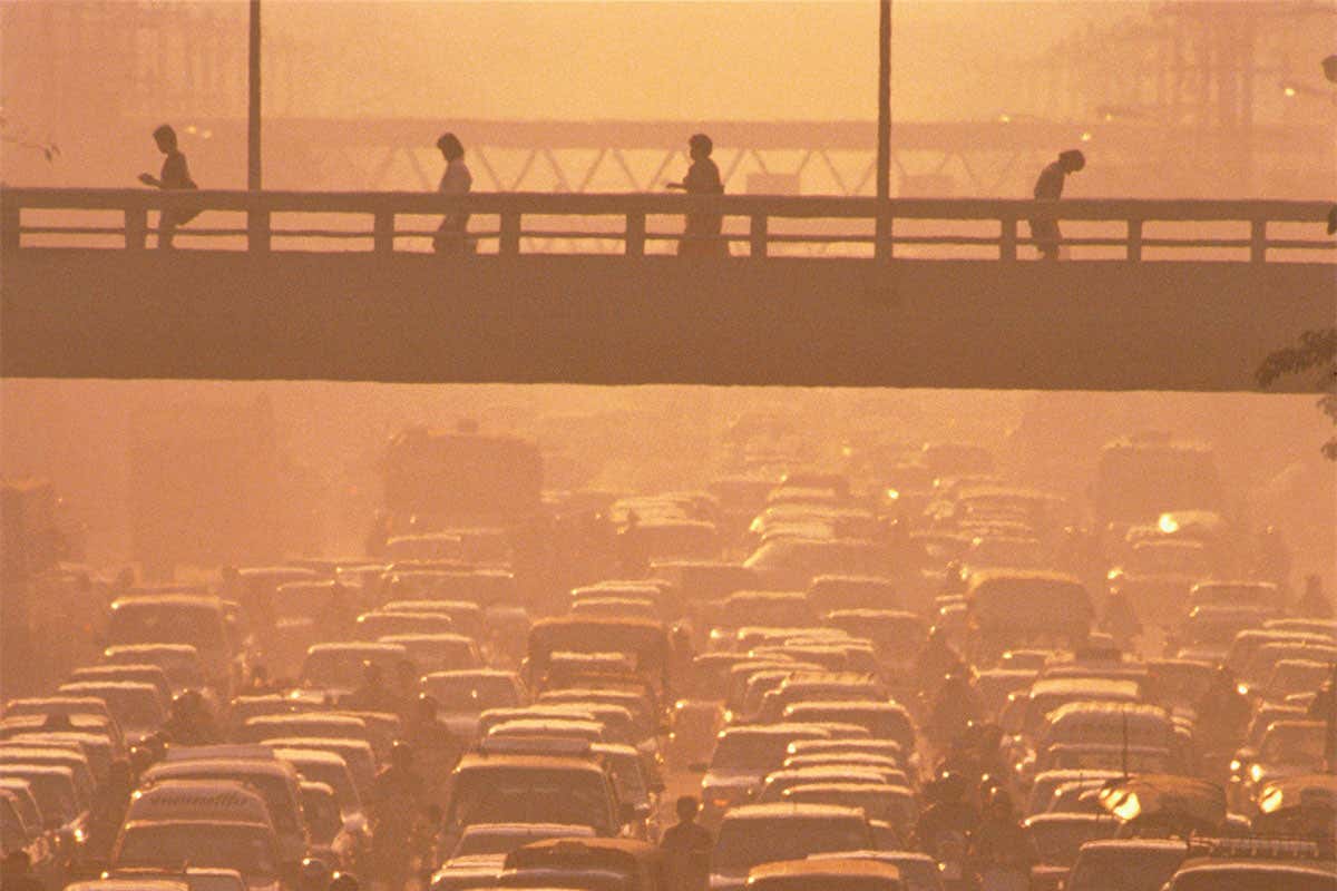 Pedestrians cross bridge over highway packed with cars