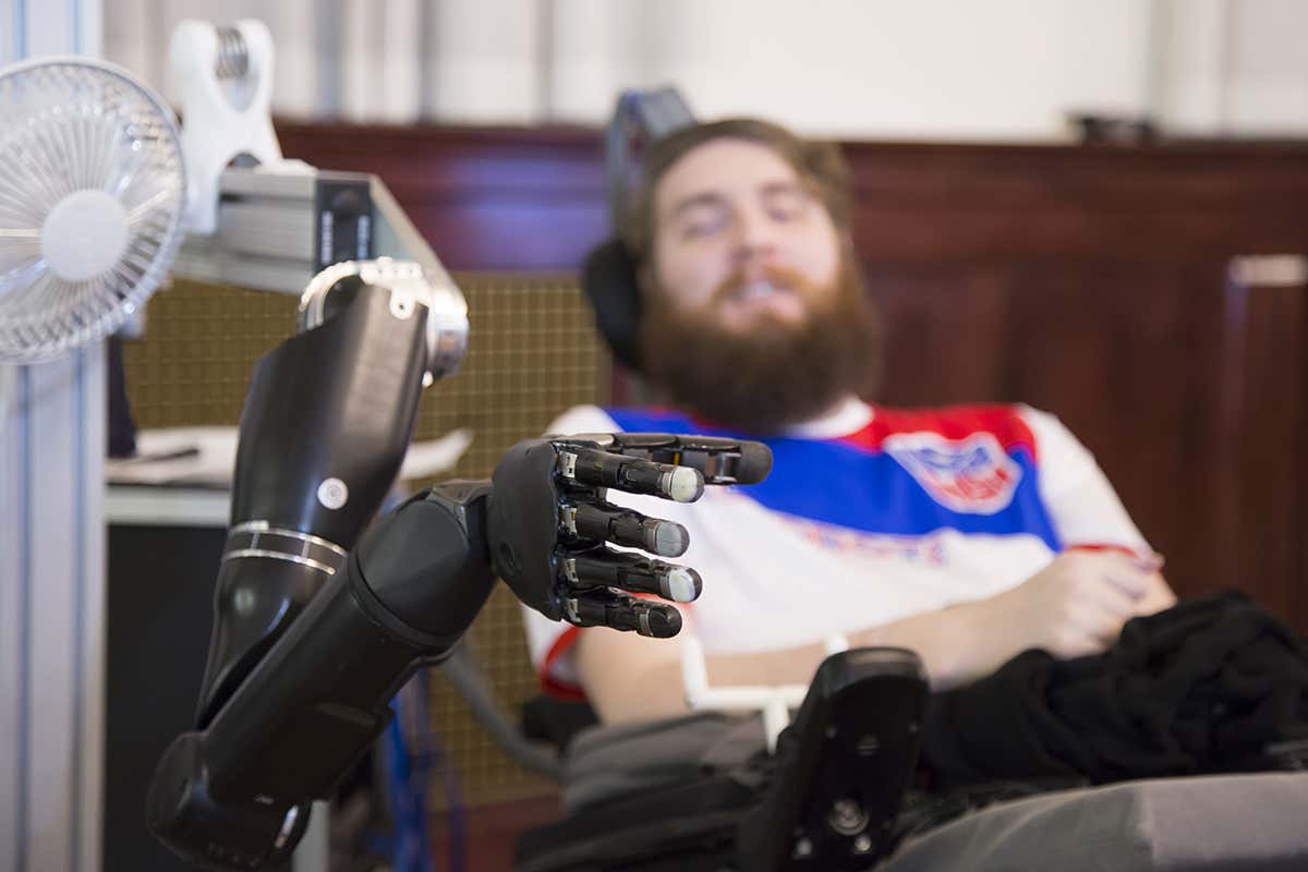 A robot hand is in the foreground and Nathan Copeland can be seen in the background