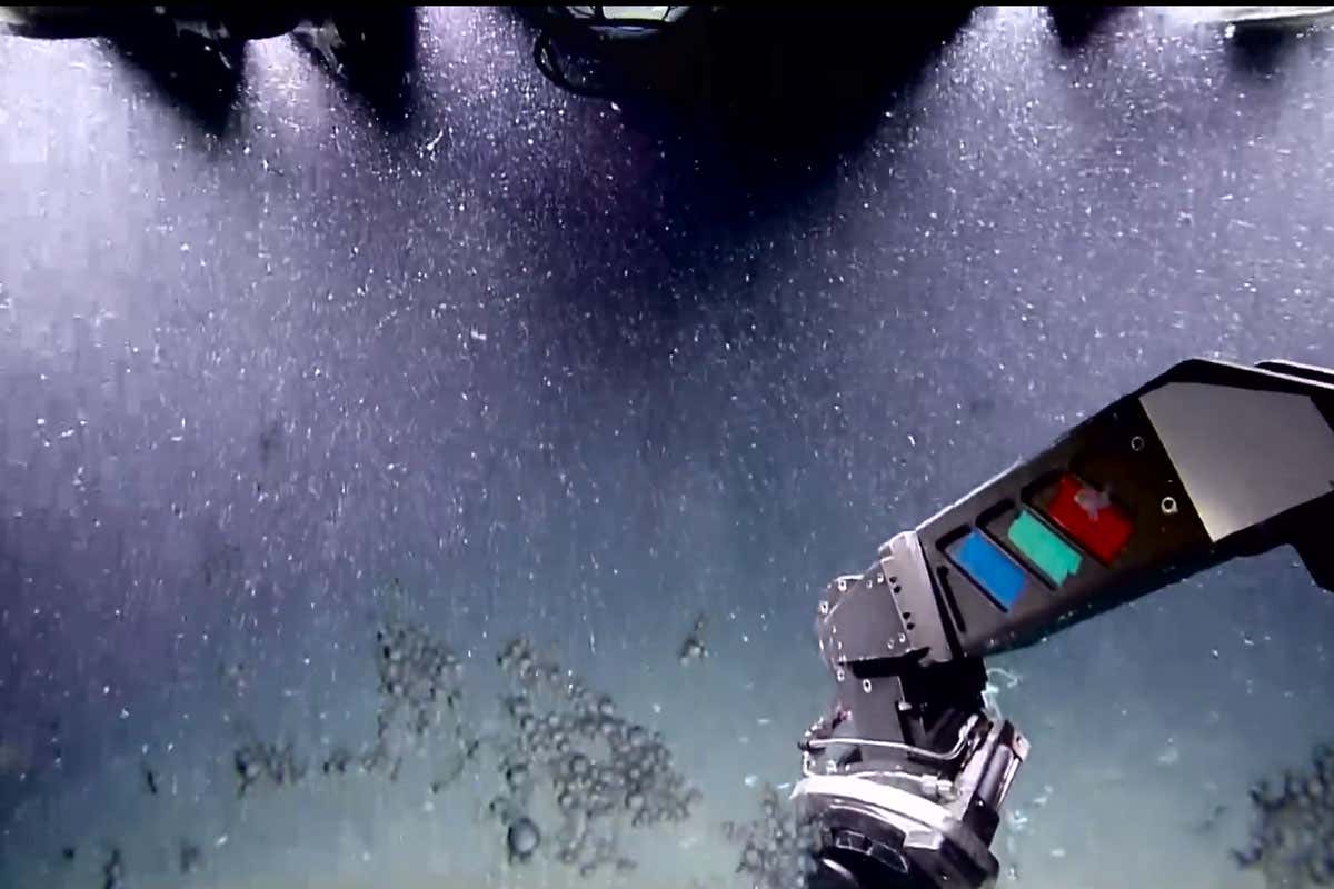 Underwater view of the seabed bubbling with methane taken by a submersible, with the submersible's arm visible in the bottom right