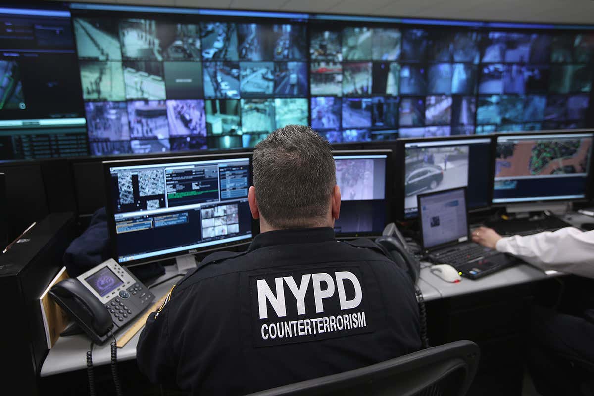 An NYPD officer sits in front of a vast array of CCTV screens