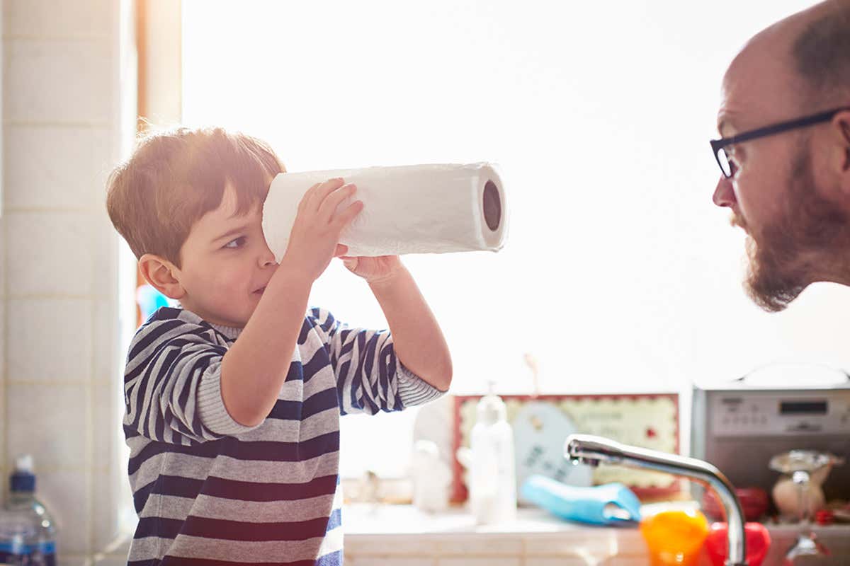 Man speaks to child who is looking down the centre of a roll of kitchen paper