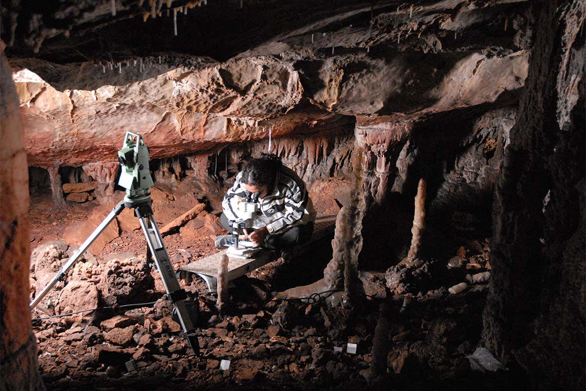 A woman bent over studying something under a microscope on the floor of a cave