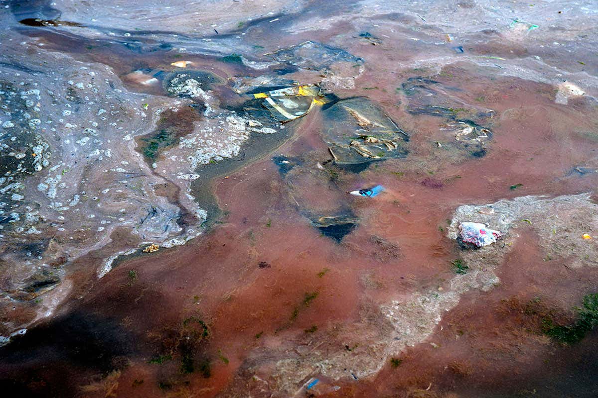 Dirty, red-tinged water with scum and rubbish floating on the surface